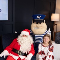 Girl in white and red dress sits with hands on legs next to Santa